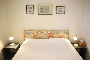 A neatly made bed with a floral headboard, two bedside lamps, and three framed artworks on the wall.