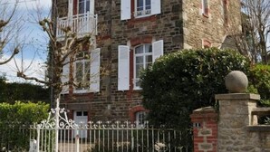 A two-story stone building with a balcony, a chimney, and a gated entrance. - Authentic Captain's house in the long courtyard of the late 19th century (Saint-Briac-Sur-Mer)