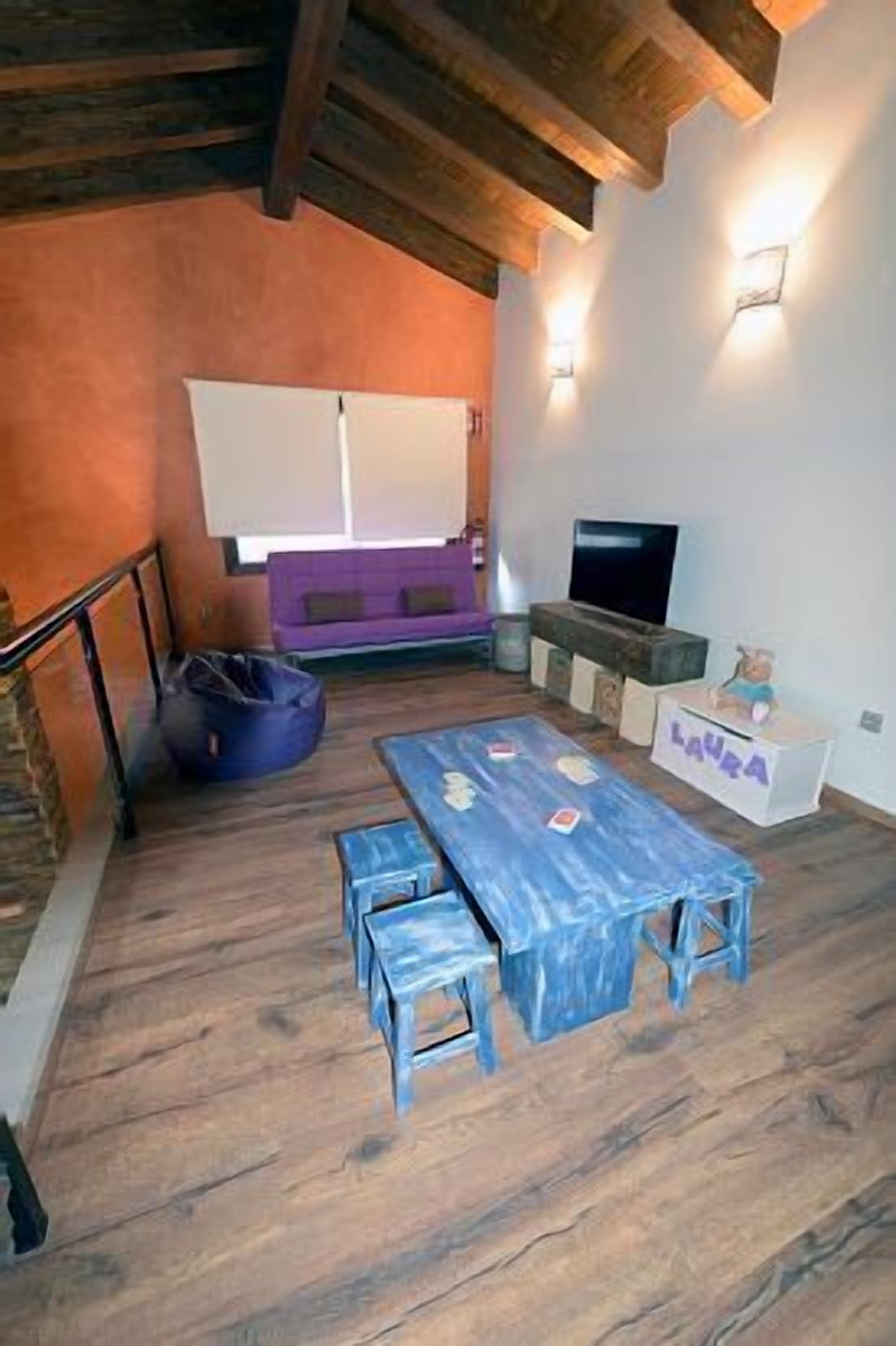 A cozy room with a wooden floor, a blue table with benches, a purple sofa, a TV, and a white cabinet with the name 'Laura'.