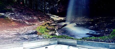 Un jacuzzi en un área boscosa, con una cascada al fondo.