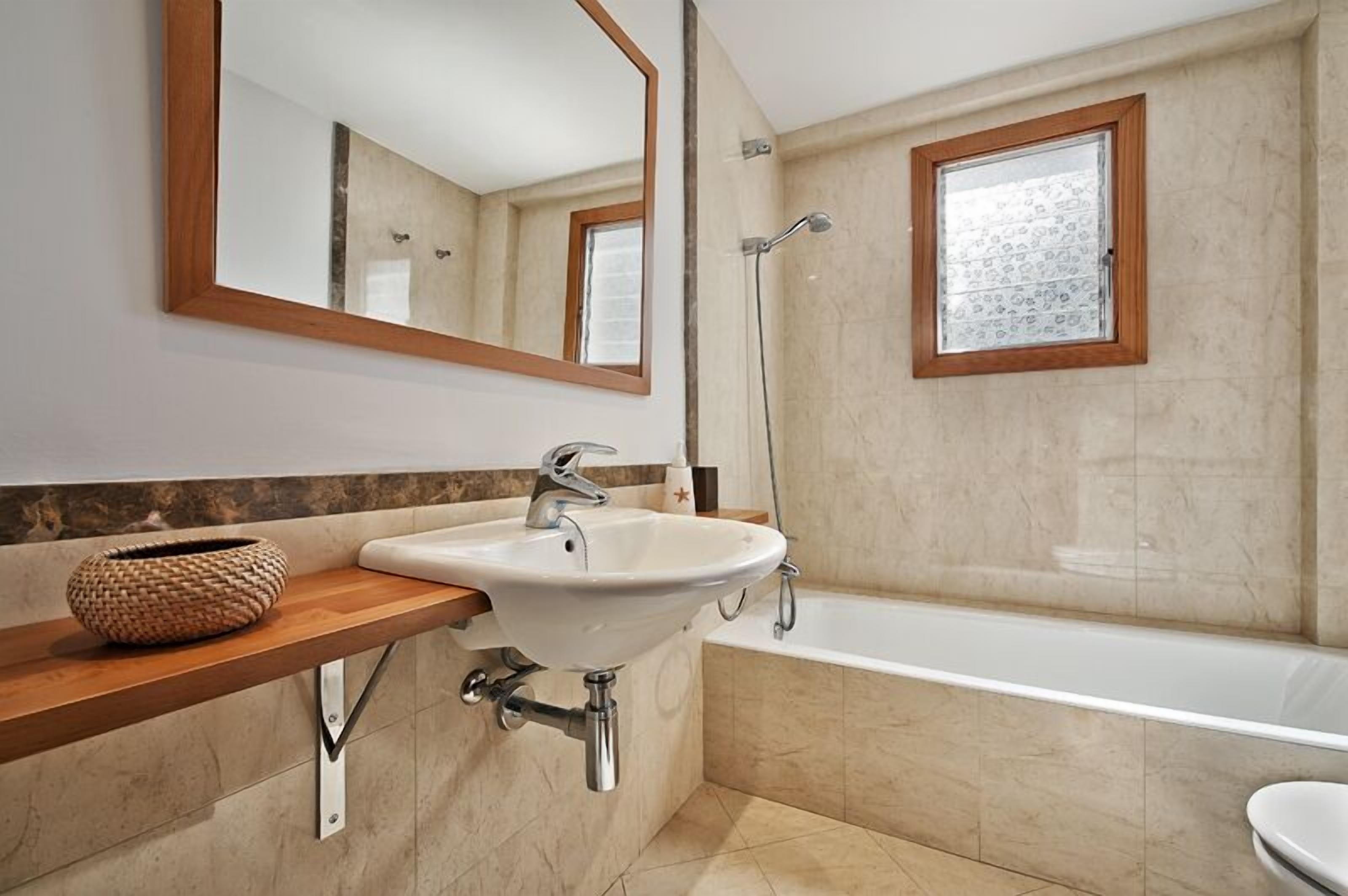 Une salle de bain moderne avec un lavabo blanc, un meuble-lavabo en bois, un grand miroir, une douche et une fenêtre.