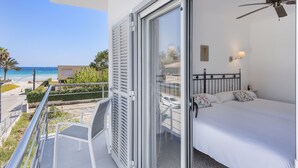 Een balkon met uitzicht op het strand en de oceaan, een bed met wit beddengoed en een plafondventilator.