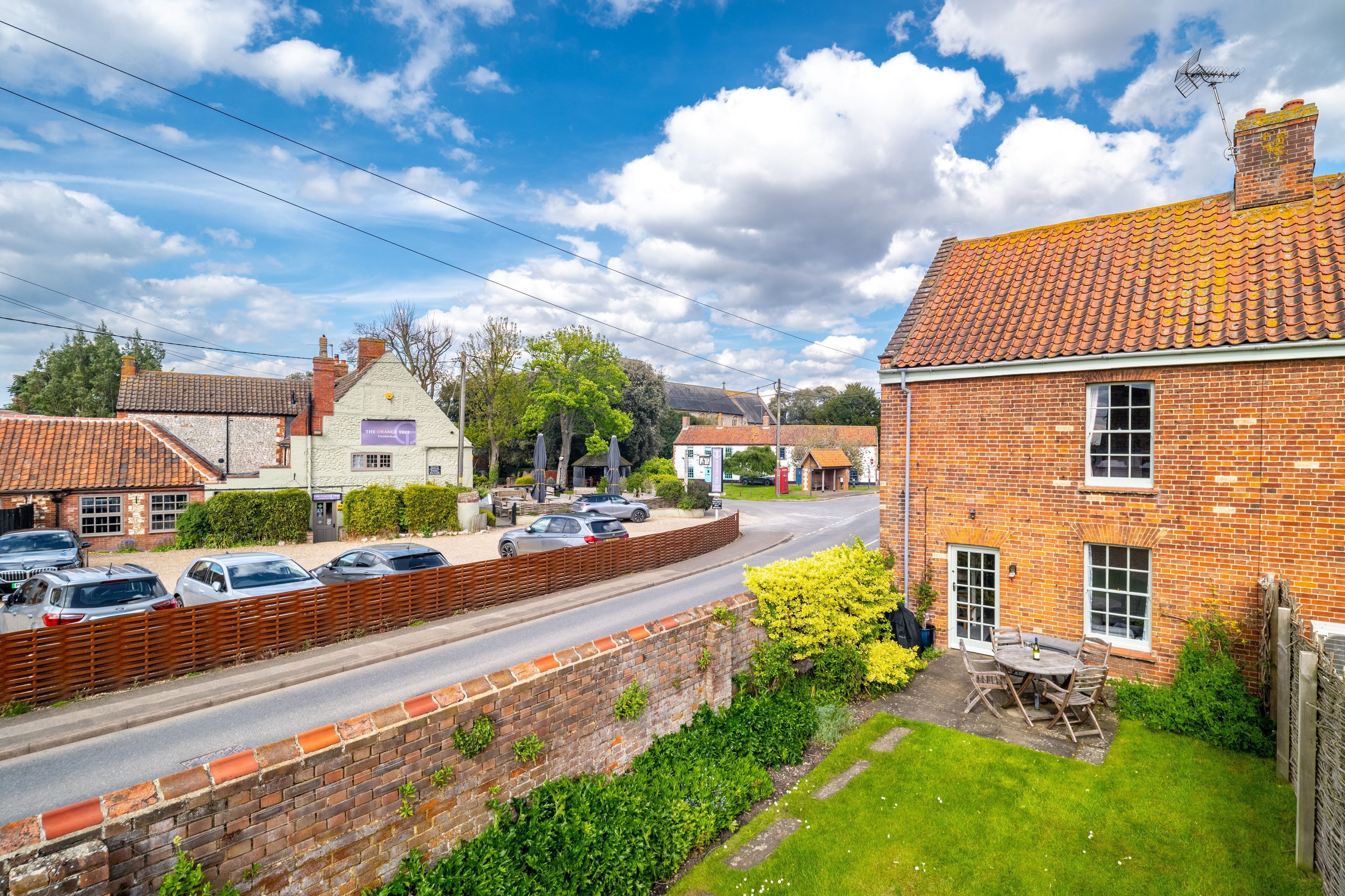 A brick house with a tiled roof, a paved driveway, and a small garden with a table and chairs.