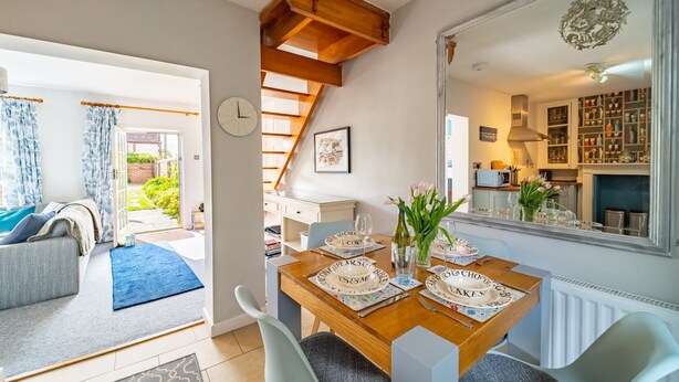 A dining area with a wooden table set for four, a staircase, and a kitchen visible through an open door.
