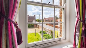 A window with a view of a residential area, curtains, and a glimpse of a garden.
