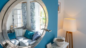 A round mirror with a nautical theme, a sofa with patterned cushions, a lamp, and a small table with a bowl.