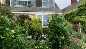 A two-story house with a stone facade, large windows, and a garden with various plants and flowers. - Durham, 3 bedroom Cottage in village location near Durham city,  pet friendly (Sherburn Village)