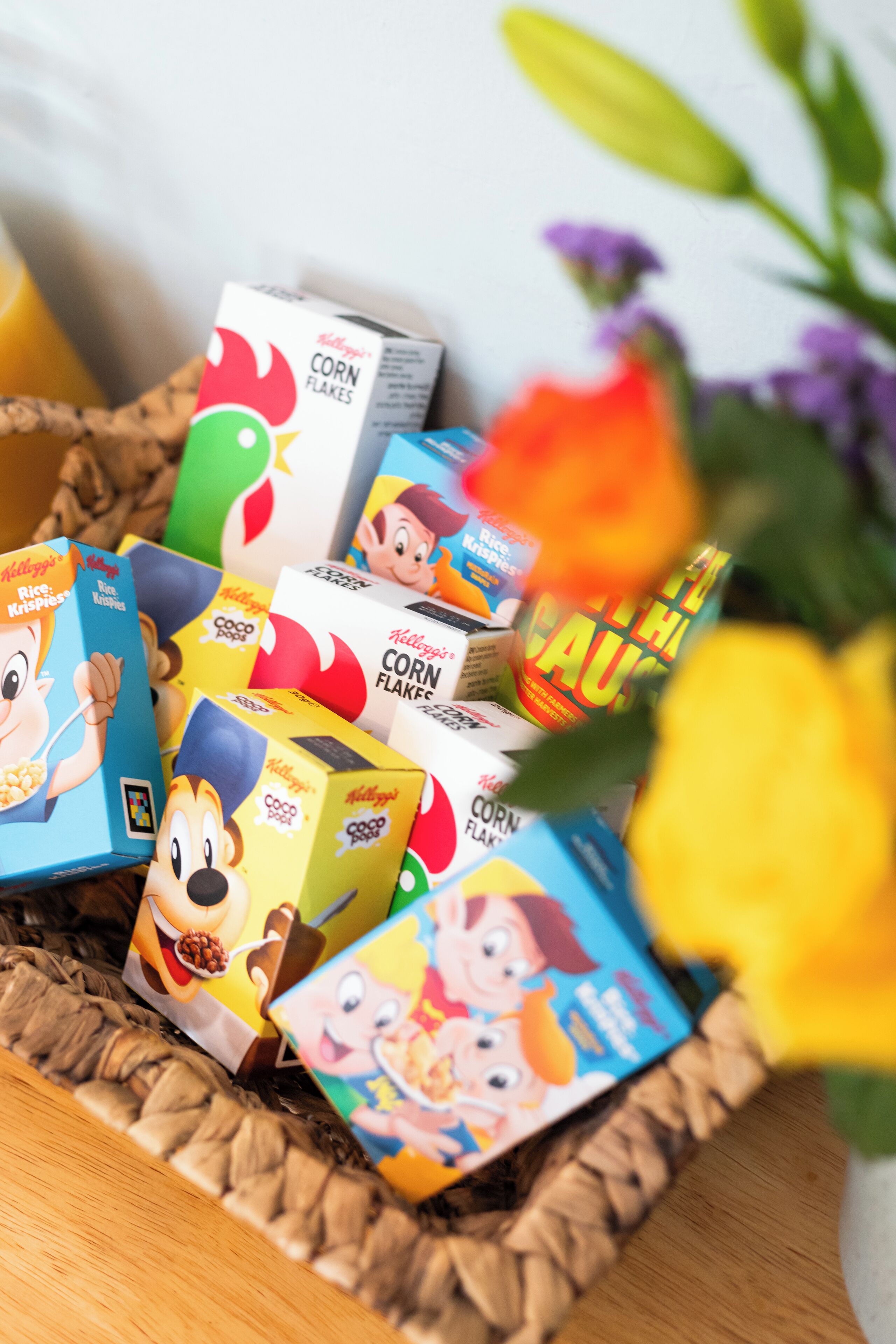 A basket filled with cereal boxes, including brands like Kellogg's and Coco Pops, placed on a wooden surface.