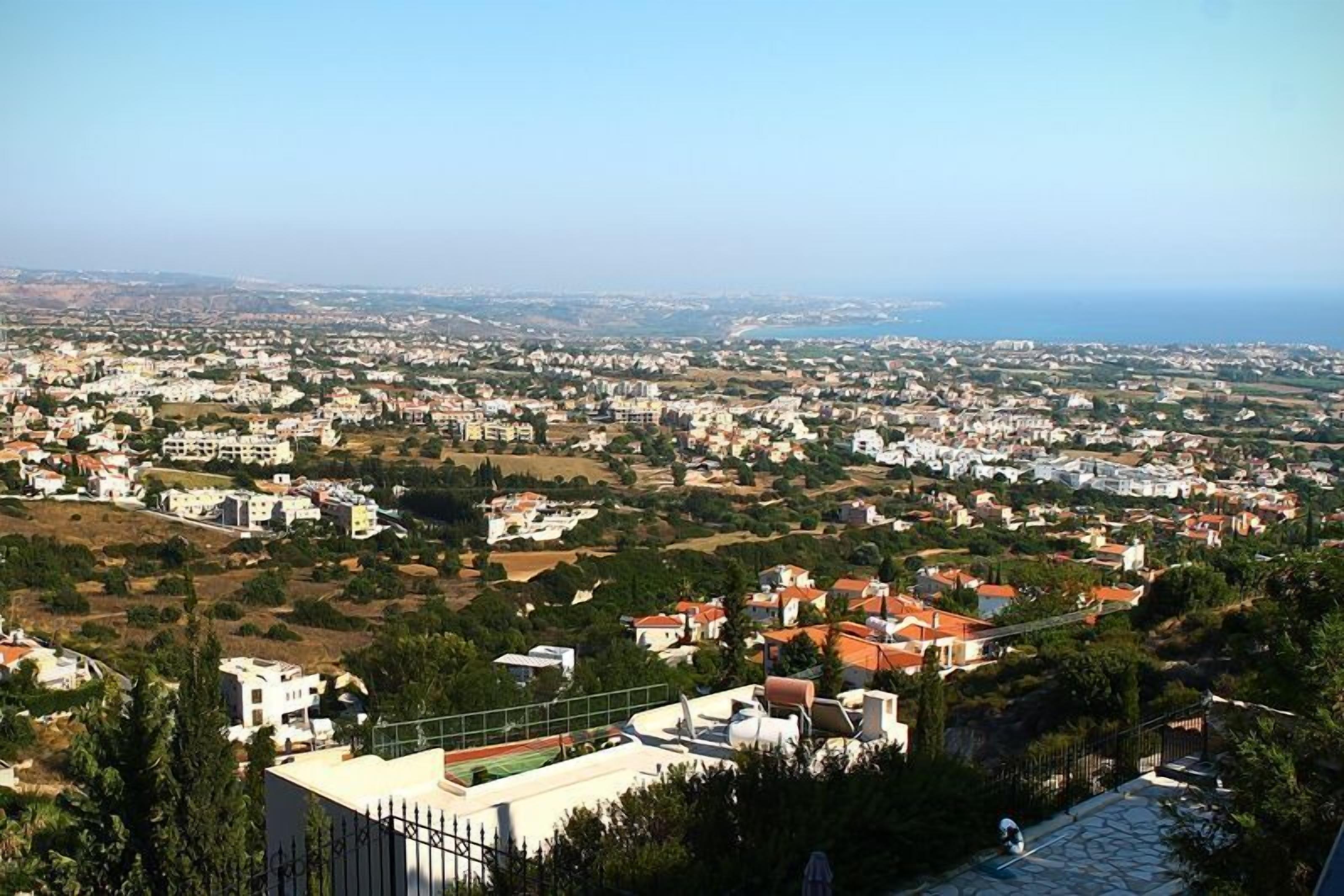A panoramic view of a coastal town with residential buildings, green spaces, and a clear view of the sea.