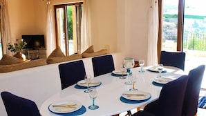 Un coin repas avec une table ronde dressée pour quatre personnes, des chaises et un téléviseur en arrière-plan.