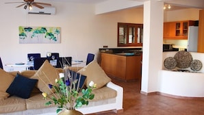 Un salon avec un canapé, un coin repas avec une table et des chaises, une cuisine avec des meubles en bois et un ventilateur de plafond.