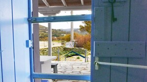 Une porte-fenêtre donnant sur un patio extérieur, doté d’un sol en pierre et offrant une vue sur une colline.