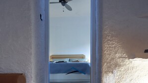 Un escalier étroit mène à une chambre à coucher équipée d’un lit, d’un ventilateur de plafond et offrant une vue sur l’extérieur.