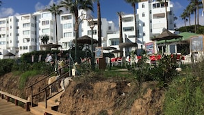 A coastal hotel with multiple white buildings, palm trees, and a wooden boardwalk leading to a sandy area. - EASY WALK TO MAX BEACH LOVELY APT  WI-FI  STUNNING SEA/POOL VIEWS +ELEVATOR/LIFT (Riviera del so/l La cala)