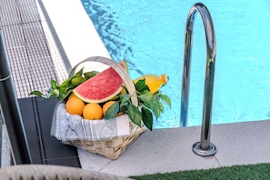 Zona de piscina con una escalera metálica, una cesta de mimbre llena de frutas y una bebida, y un camino empedrado.