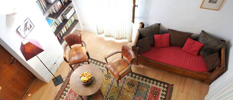 Un salon comprenant un canapé, des fauteuils, une table basse, une bibliothèque et un tapis à motifs.