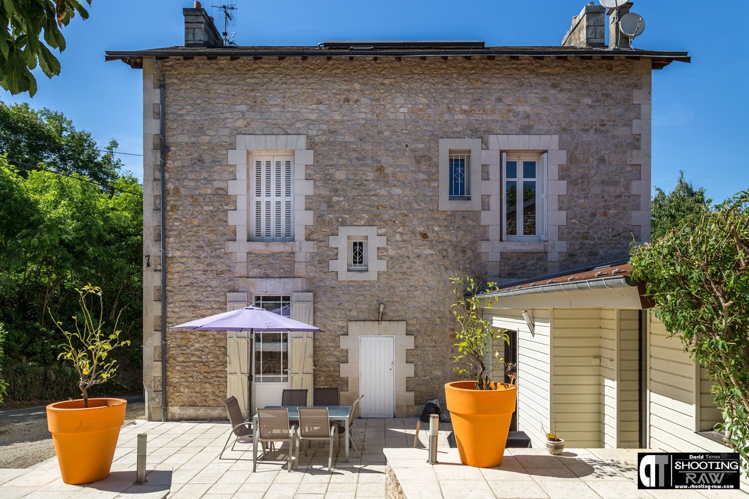 Un bâtiment en pierre doté d’un patio, de sièges en plein air et de plantes en pot.