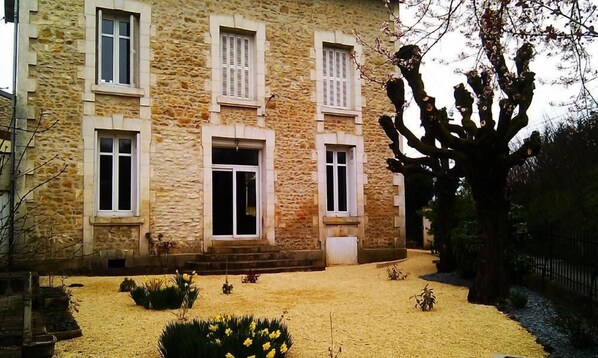A stone building with a central entrance, multiple windows, and a garden with yellow flowers and a tree. - House / Villa - POITIERS (Poitiers)