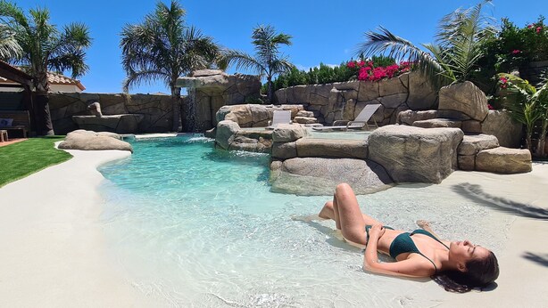 A pool area with clear water, rocks, and palm trees.