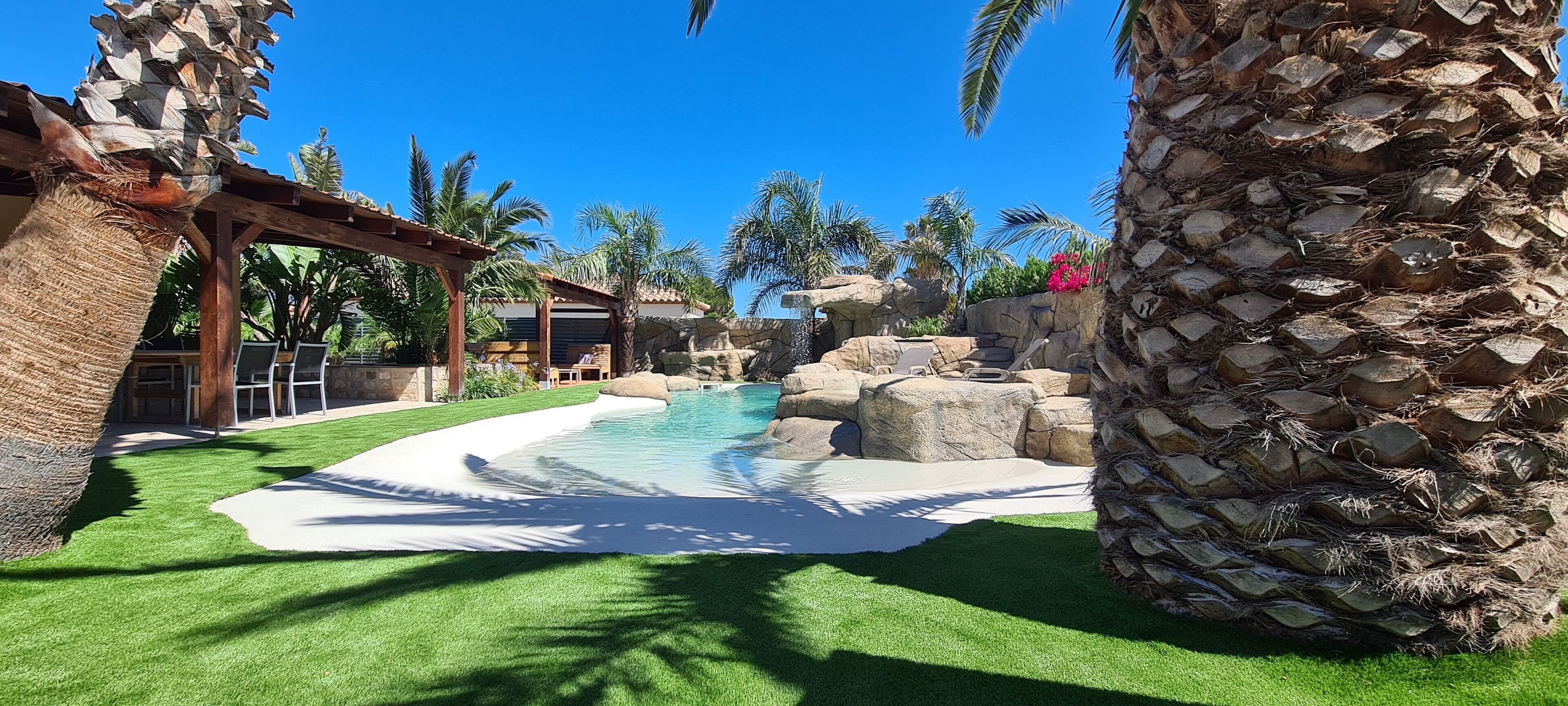 A pool area with artificial grass, palm trees, and a stone wall.