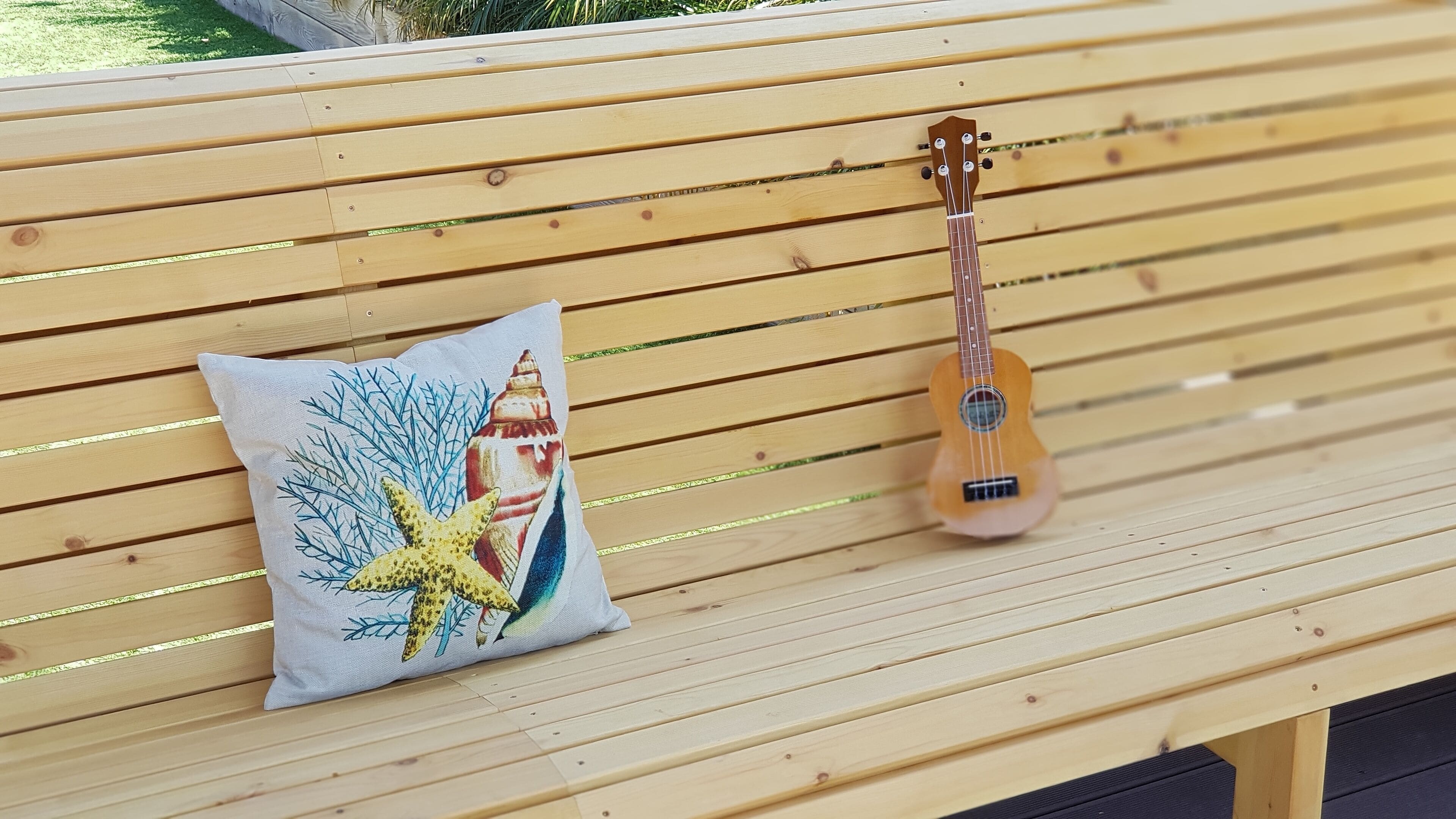 A wooden bench with a pillow and a ukulele.