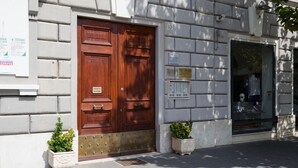 Un bâtiment doté d’une grande porte à double battant en bois, de plantes en pot et d’une fenêtre où est placé un mannequin.