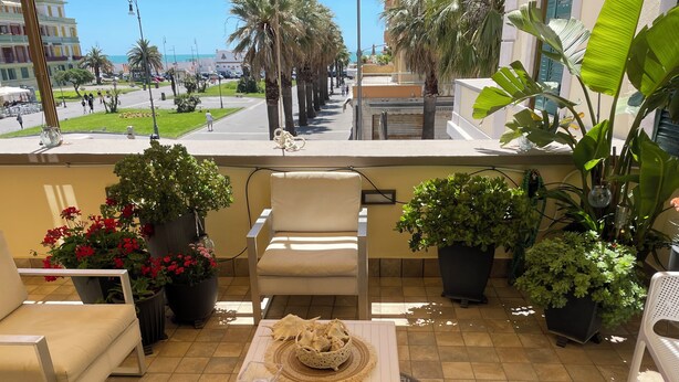 Un balcon avec une table, des chaises, des plantes en pot et une vue sur la rue et les immeubles.