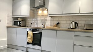 Eine moderne Küche mit weißen Schränken, einer Edelstahl-Dunstabzugshaube, einer Mikrowelle, einem Backofen und einem Wasserkocher auf der Arbeitsplatte.