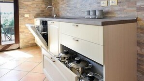 Une cuisine compacte avec des meubles blancs, une cuisinière encastrée et un pare-feu en pierre.
