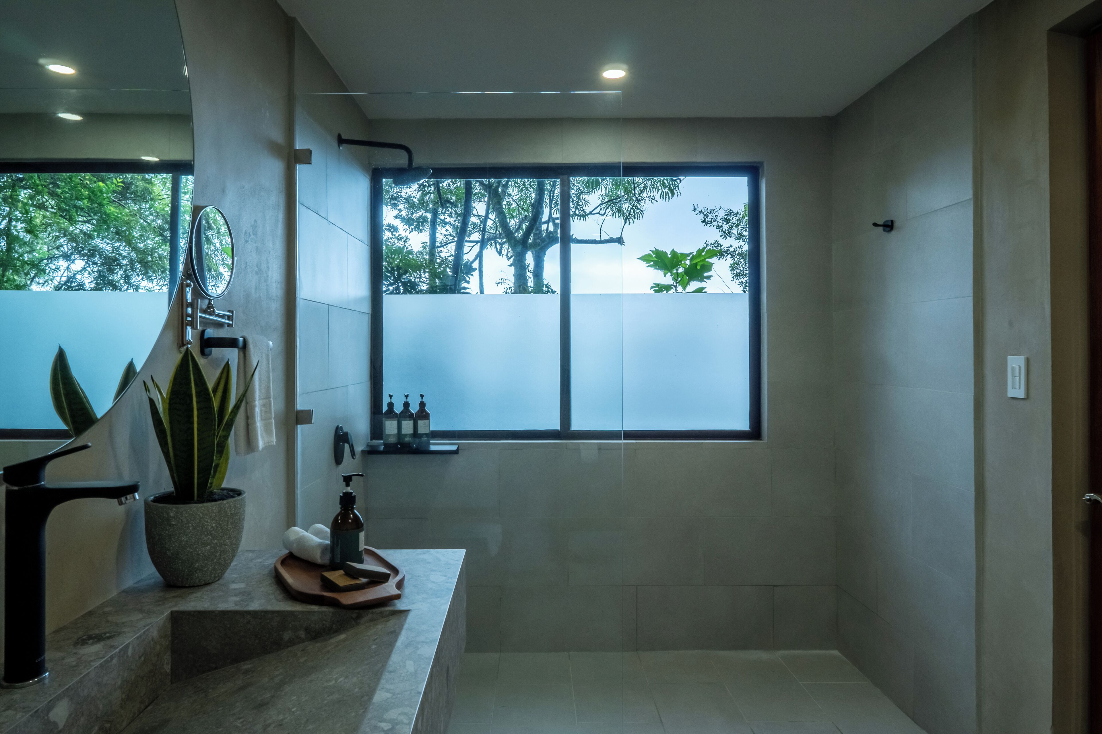 Une salle de bain moderne avec une grande fenêtre, une plante en pot et un miroir.