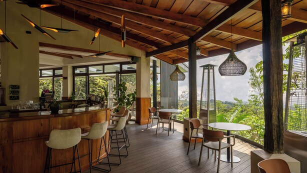 A spacious outdoor bar area with wooden flooring, bar stools, and hanging pendant lights. - Koora Hotel by Sandglass (Monteverde)