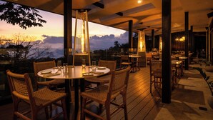 An outdoor dining area with wicker chairs and tables, large windows overlooking a scenic view, and modern lighting fixtures. - Koora Hotel by Sandglass (Monteverde)