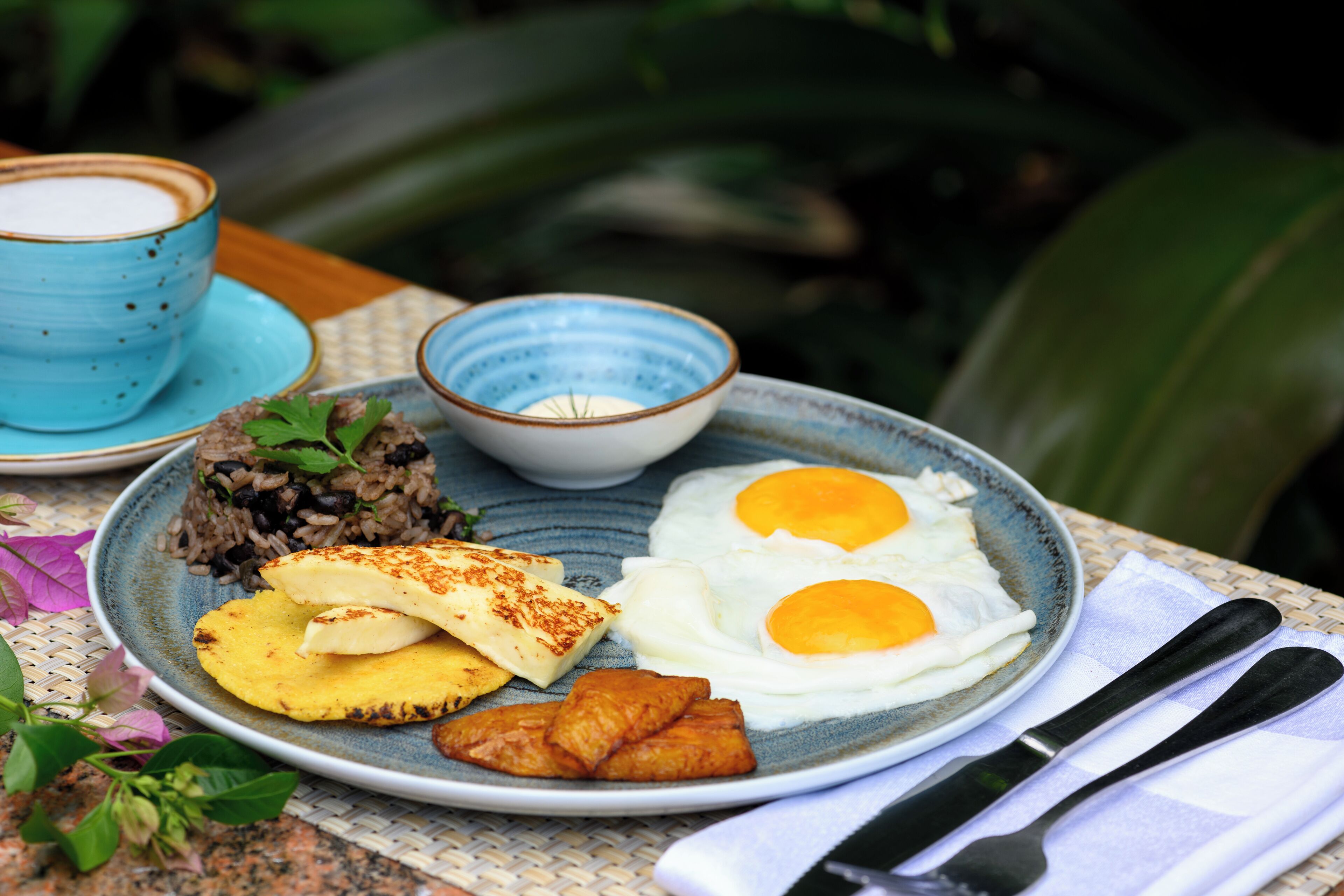 Un plato de comida con arroz, huevos, plátanos maduros y plátanos fritos, servido en un plato de cerámica azul.