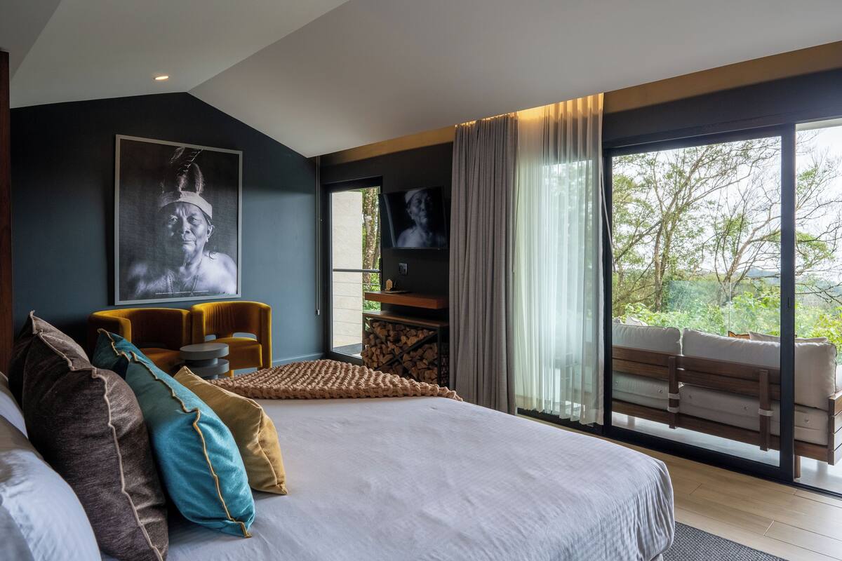 A modern bedroom with a large bed, a view of the outdoors, and a mounted TV.