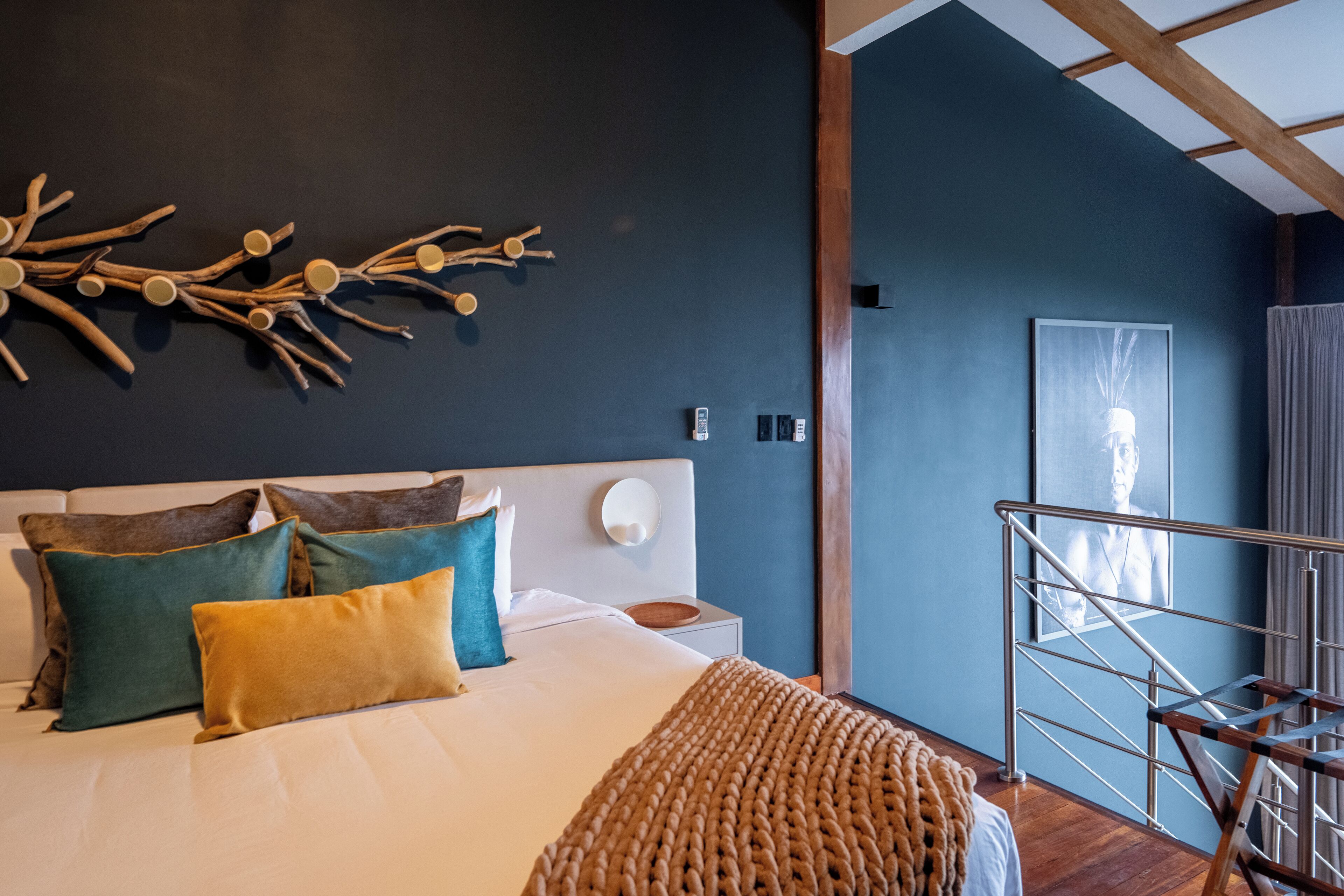 Un dormitorio con cama, almohadas, una obra de arte en la pared, una mesita de noche y una escalera.