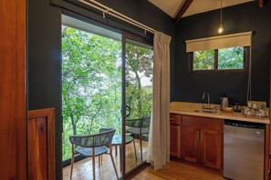 A kitchen with a view of greenery, a dining area with chairs, and a sliding glass door.