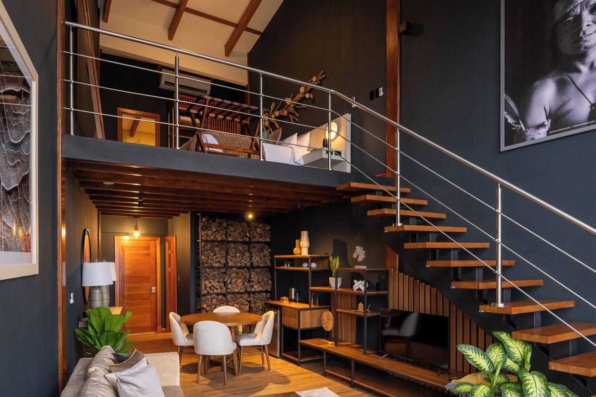 A modern loft with a wooden staircase, a dining area, and a living space with a large plant.