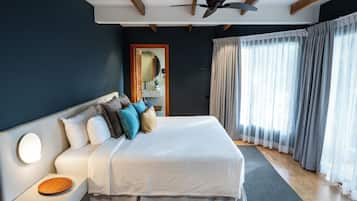 A modern bedroom with a large bed, a nightstand, a ceiling fan, and a view of the outdoors through sheer curtains.