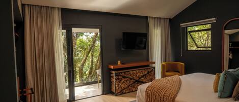 Un dormitorio con cama, televisión, escritorio y silla, y ventana con vista a árboles.