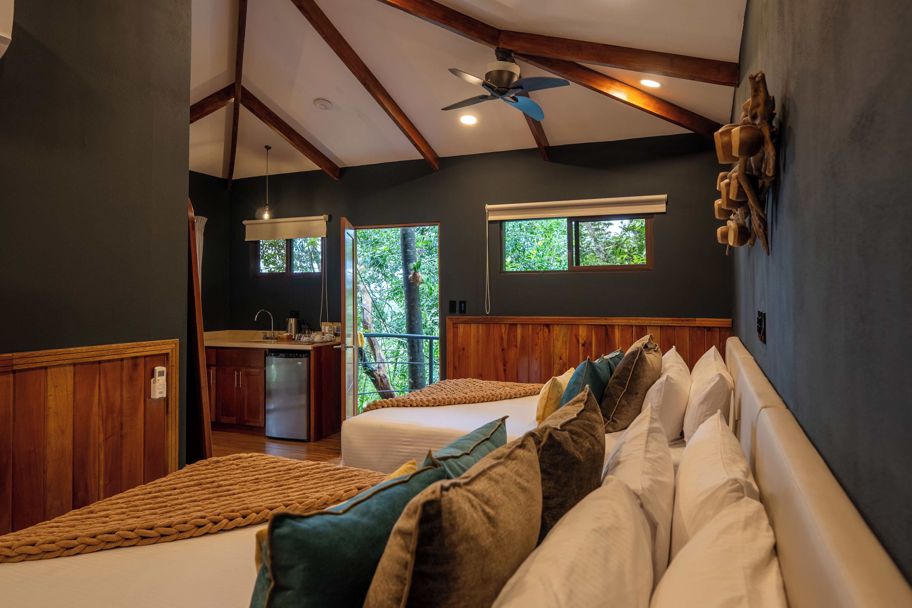 A bedroom with two beds, a wooden ceiling, and a view of the outdoors.