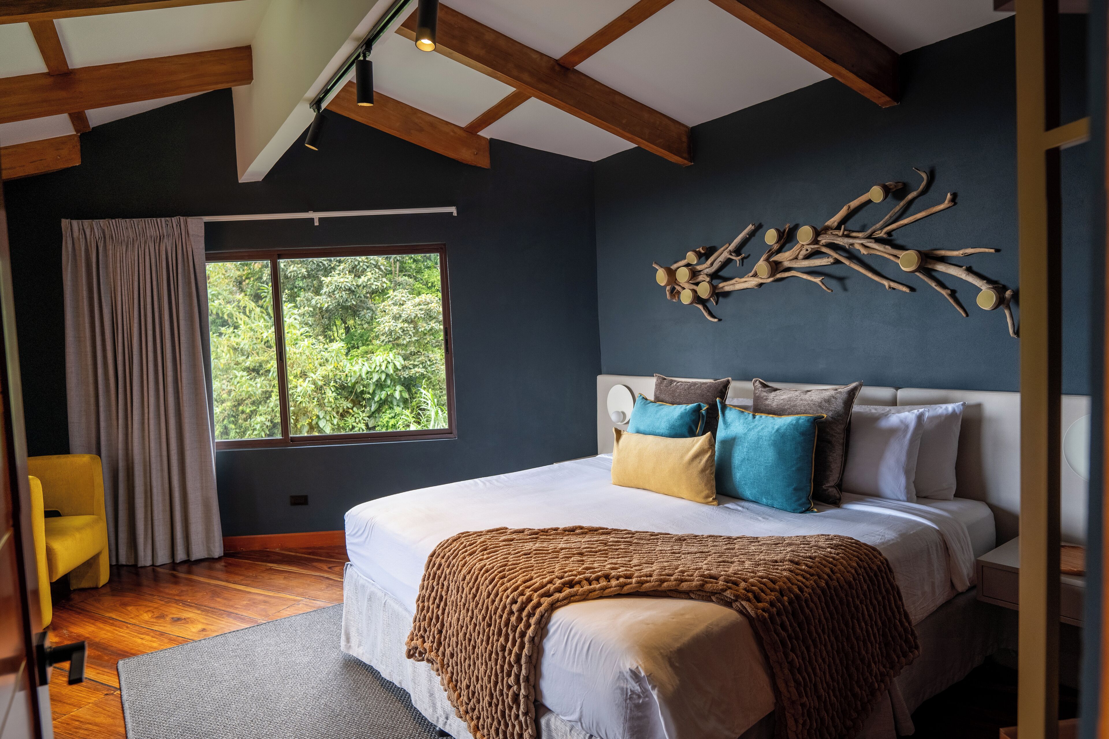 A bedroom with a large bed, a wooden ceiling, a window with curtains, and a wall-mounted decor piece.