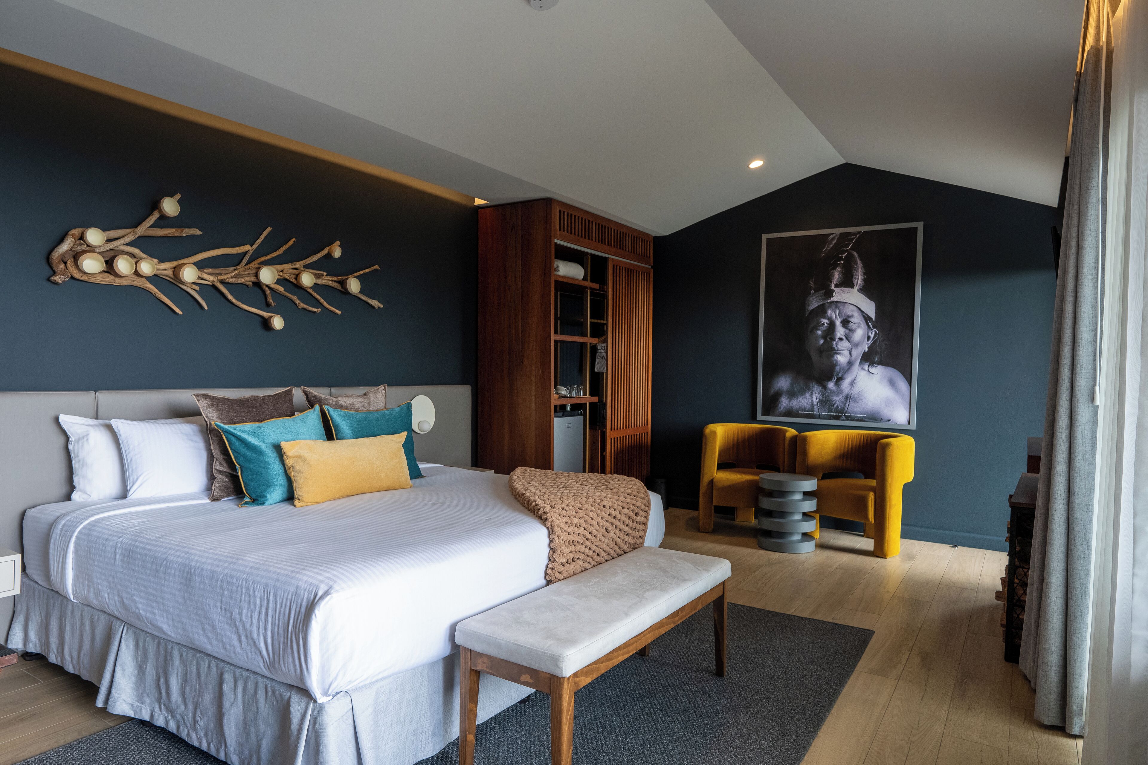 Un dormitorio moderno con una cama grande, un banco, un armario de madera y una pieza de arte única en la pared.