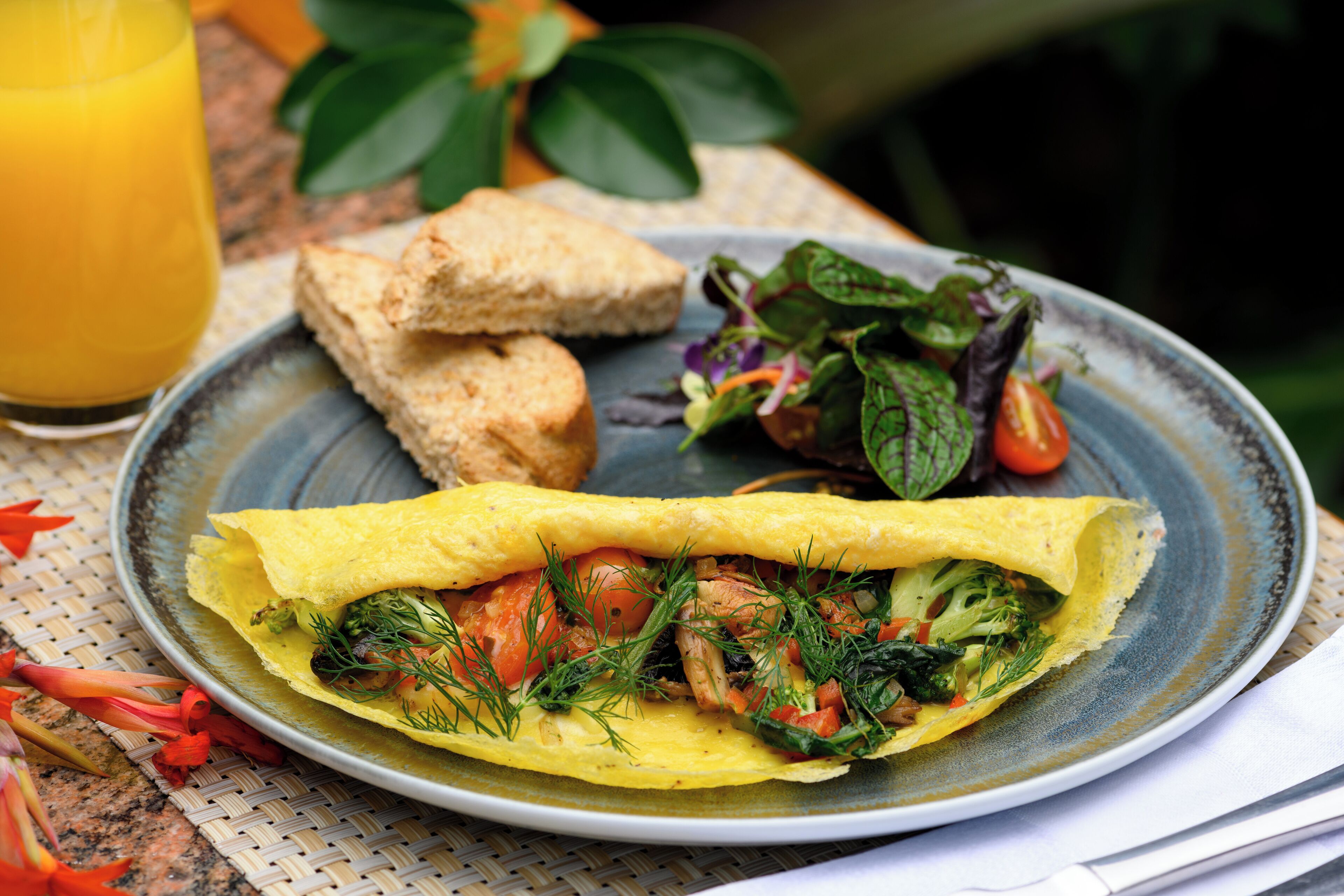 A plate with a rolled omelette, a side salad, and toast, accompanied by a glass of orange juice.