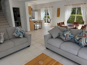 A modern living room with two grey sofas, a wooden coffee table, and a kitchen area in the background.