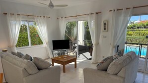 Una sala de estar con dos sofás, una mesa de centro, un televisor y un balcón con vista a la piscina.