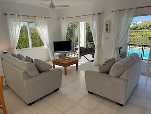 Un salon avec deux canapés, une table basse, un téléviseur et un balcon donnant sur la piscine.