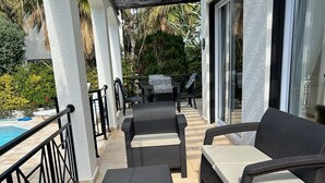 Un patio al aire libre con mobiliario de mimbre, una piscina y una zona cubierta con un pérgola.