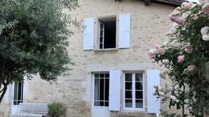 Un edificio in pietra con persiane bianche, un vialetto sterrato e una panchina.