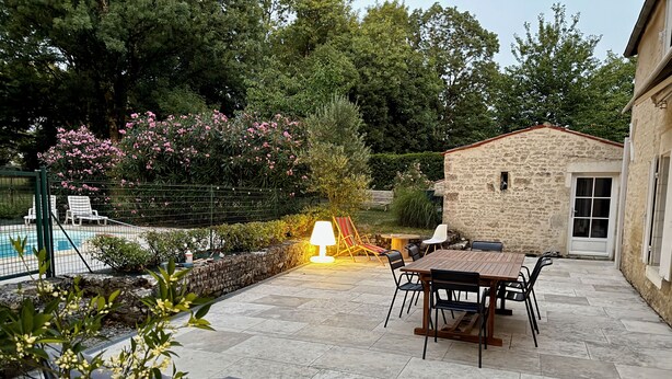 Una veranda con tavolo e sedie, un edificio in pietra e una piscina sullo sfondo.