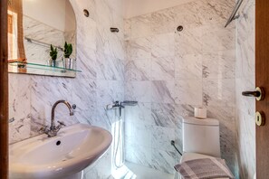 A bathroom with a marble wall, a sink, a mirror, and a shower.